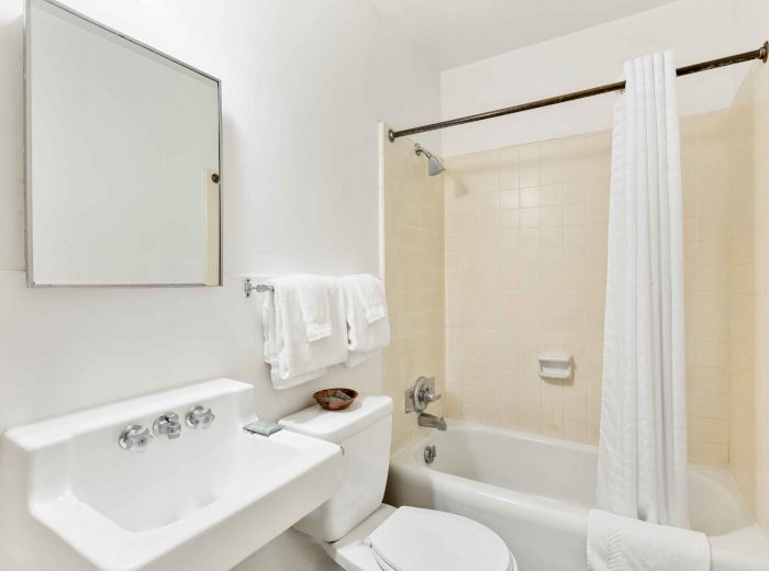 This image shows a clean, white bathroom with a mirror, sink, toilet, towels, and a bathtub with a shower curtain.
