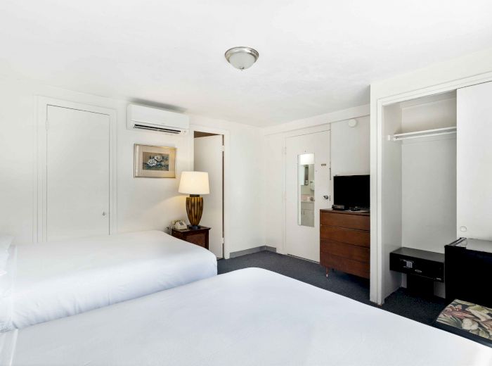 The image shows a hotel room with two beds, a dresser, a TV, a lamp, a painting, and an open closet.