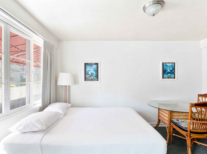 A minimalist room with a bed, glass table, wicker chairs, window, lamp, and two framed pictures on the wall is shown.