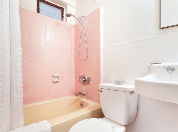 A bathroom with pink tiles, white bathtub, curtain, sink, and toilet. The ambiance is clean and minimalistic.