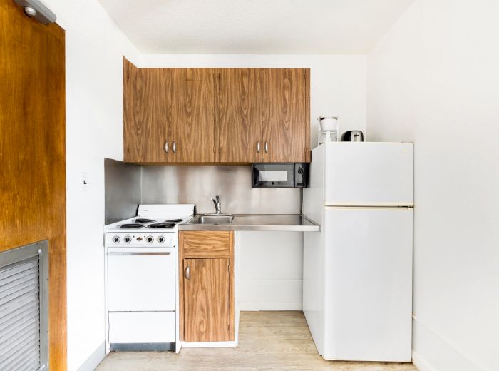 Compact kitchen with wood cabinets, a white fridge, stove, and a small sink. It features a microwave and minimal counter space.