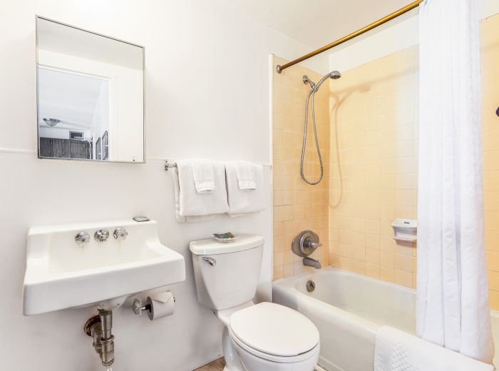 The image shows a bathroom with a sink, mirror, toilet, and a bathtub with a shower curtain and towels hanging nearby.