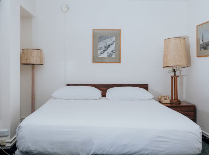 A neat bedroom with a large bed, two lamps on either side, and framed pictures on white walls.