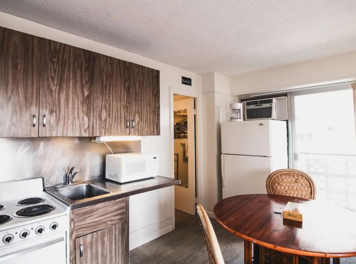 A small kitchen with a stove, sink, microwave, refrigerator, and a round dining table with chairs near a sliding door.