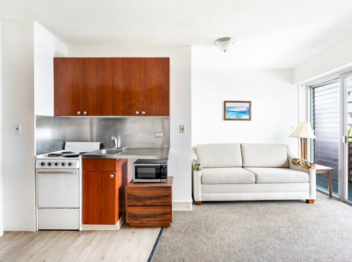 A compact living area with a kitchenette, sofa, small table, and sliding glass door leading to a balcony.