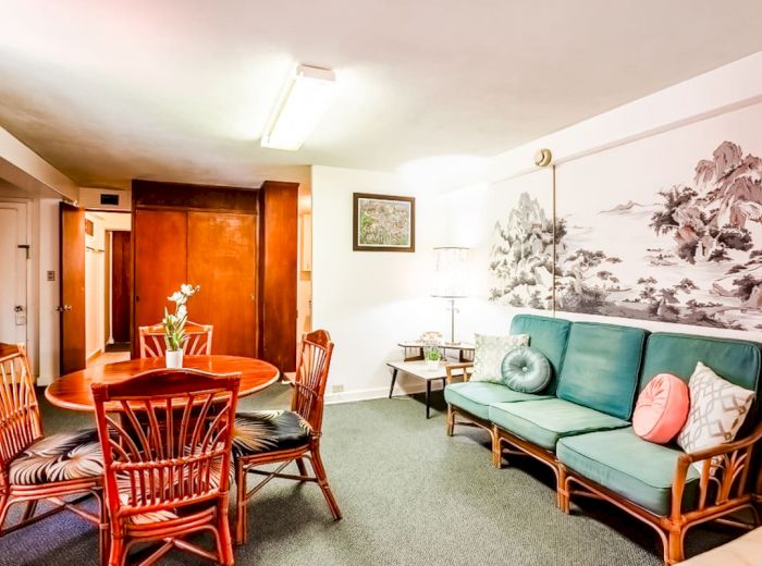 A cozy living room with a green sofa, a round wooden dining table with wicker chairs, and a large wall art piece, ends the sentence.