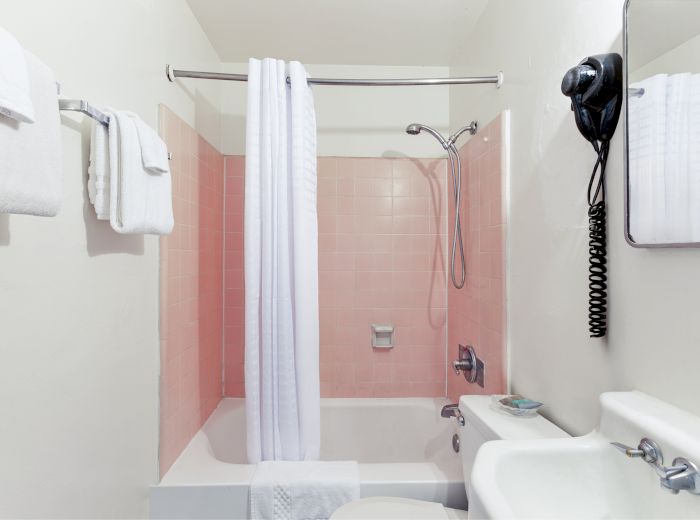 A bathroom with a pink-tiled shower, white curtain, towels, wall-mounted hairdryer, mirror, sink, and soap appears in the image.