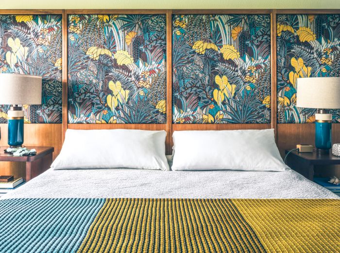 A tidy bedroom with a large bed, vibrant patterned headboard, two bedside tables with lamps, and a colorful knitted blanket on the bed.