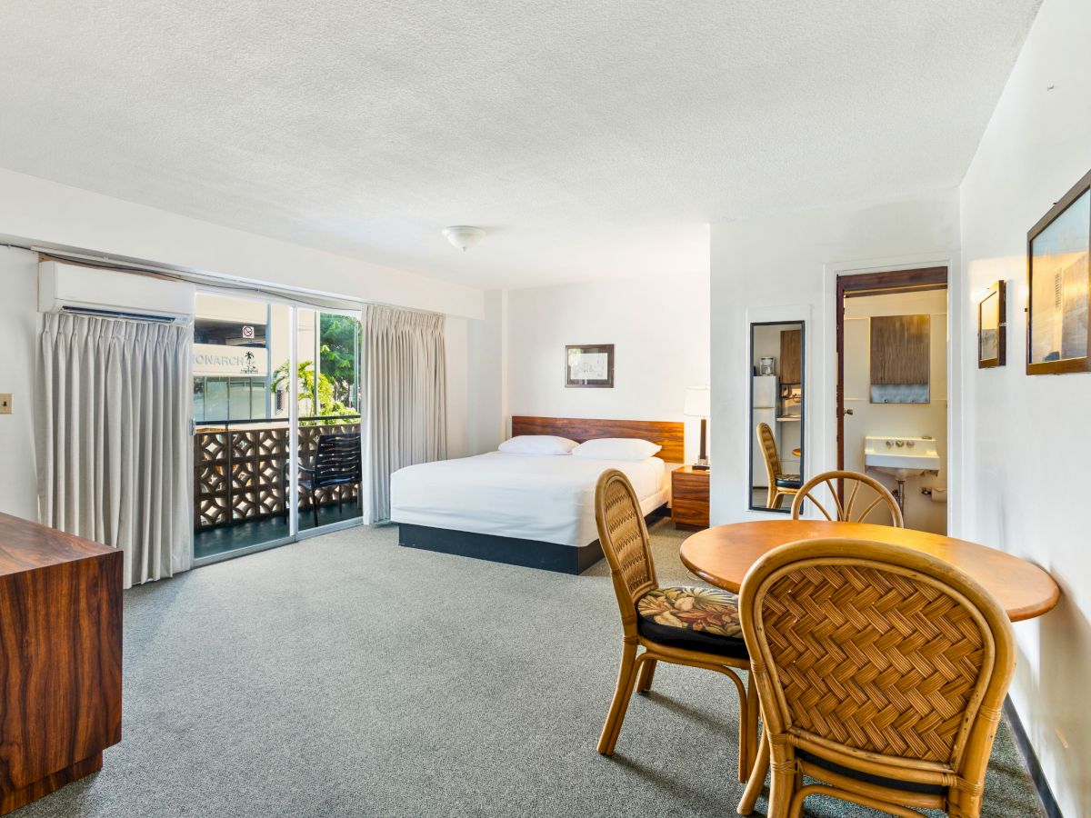A hotel room with a bed, table, chairs, dresser, and balcony.