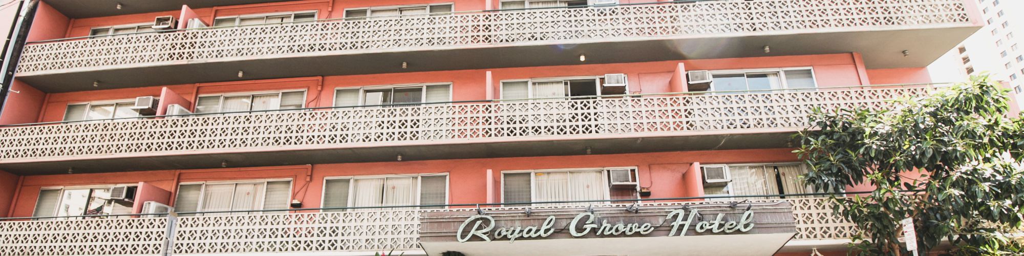 A multi-story building labeled with a hotel name, featuring balconies and a street view with a parked vehicle in front.